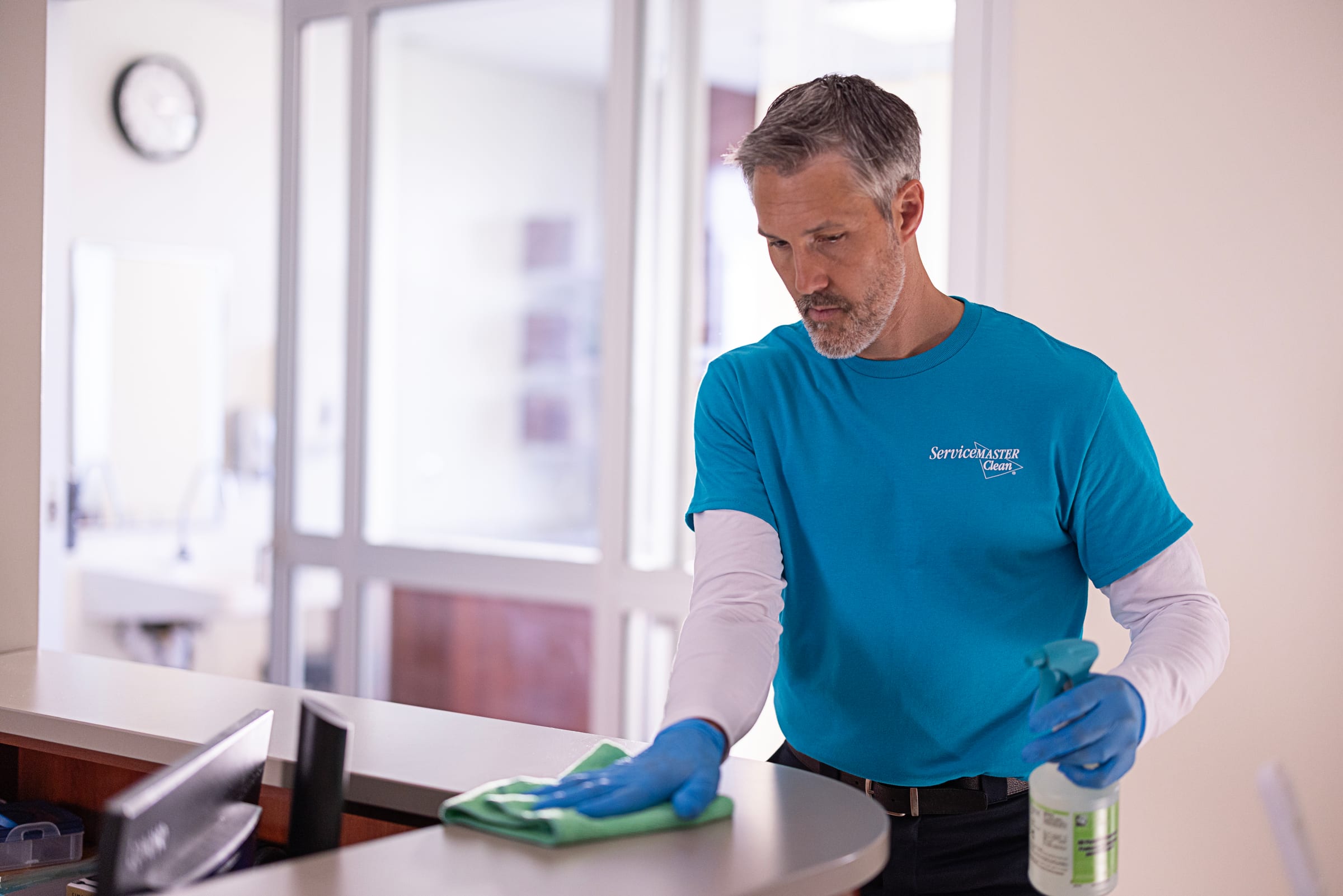 A clinical corridor with high-touch surfaces being disinfected, doors and handrails visibly treated.