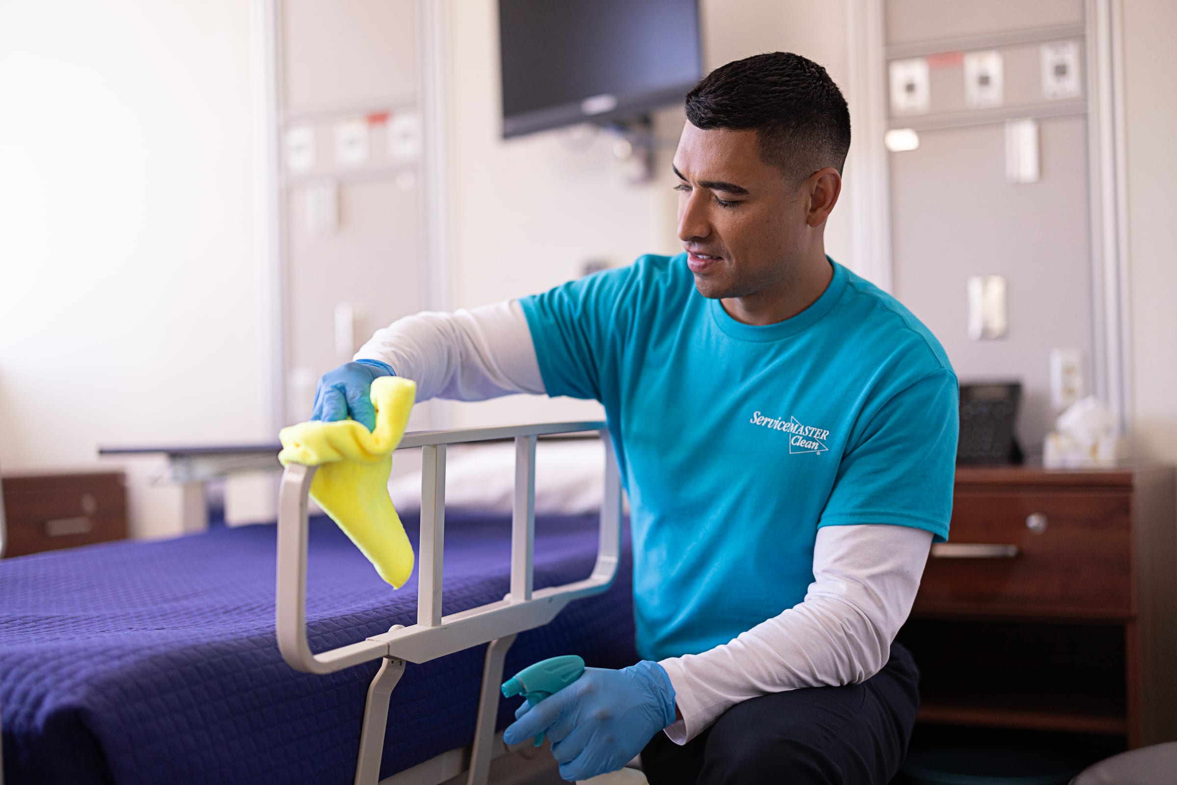A clinical corridor with high-touch surfaces being disinfected, doors and handrails visibly treated.